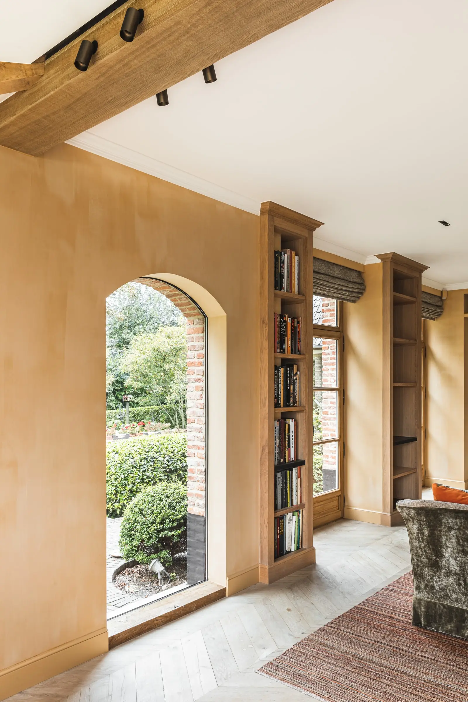 Boogdeur naar de tuin in een okerkleurige muur, naast een boekenkast