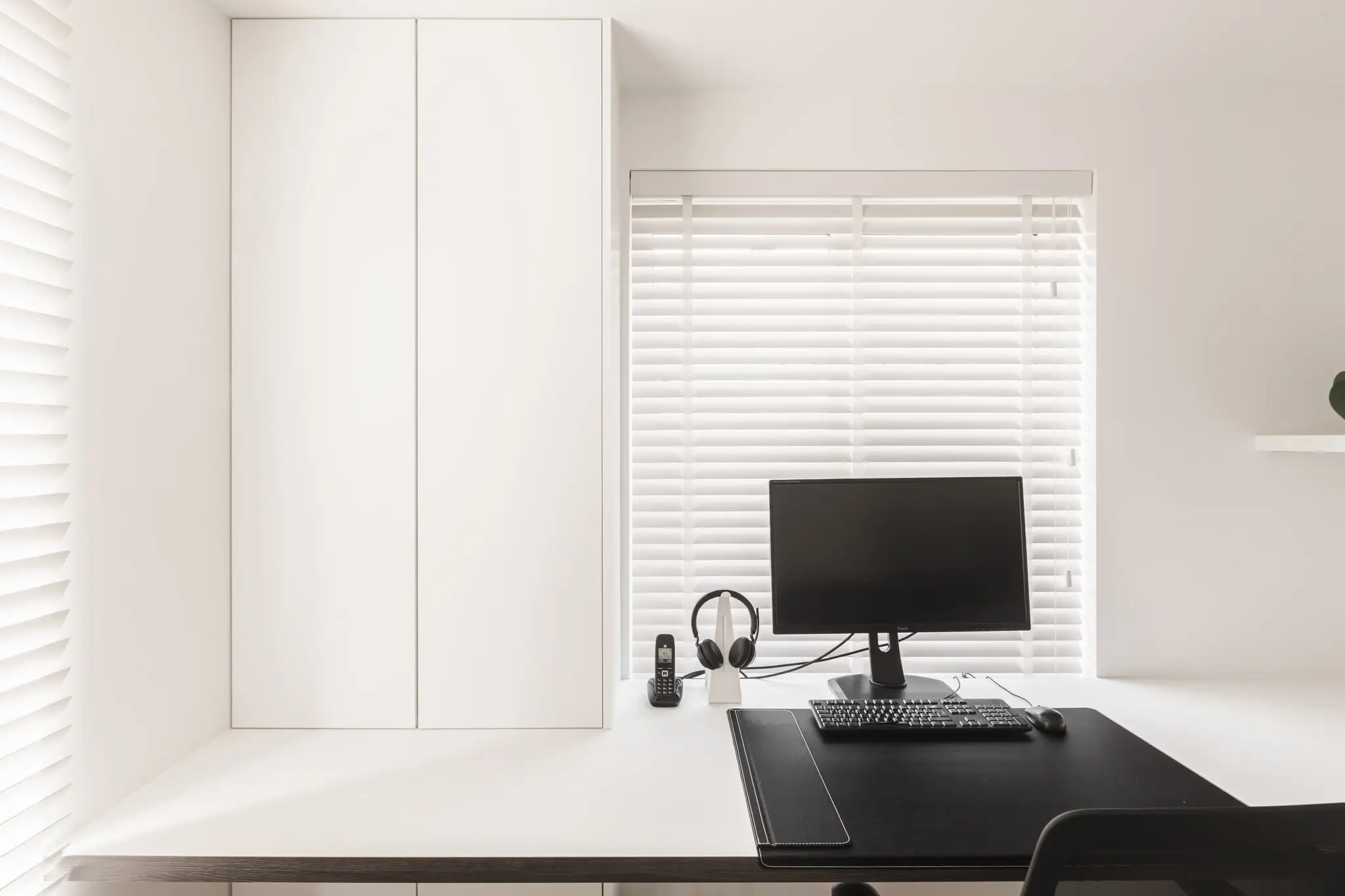 Witte bureaukamer met een zwart bureau en een raam met lamellen