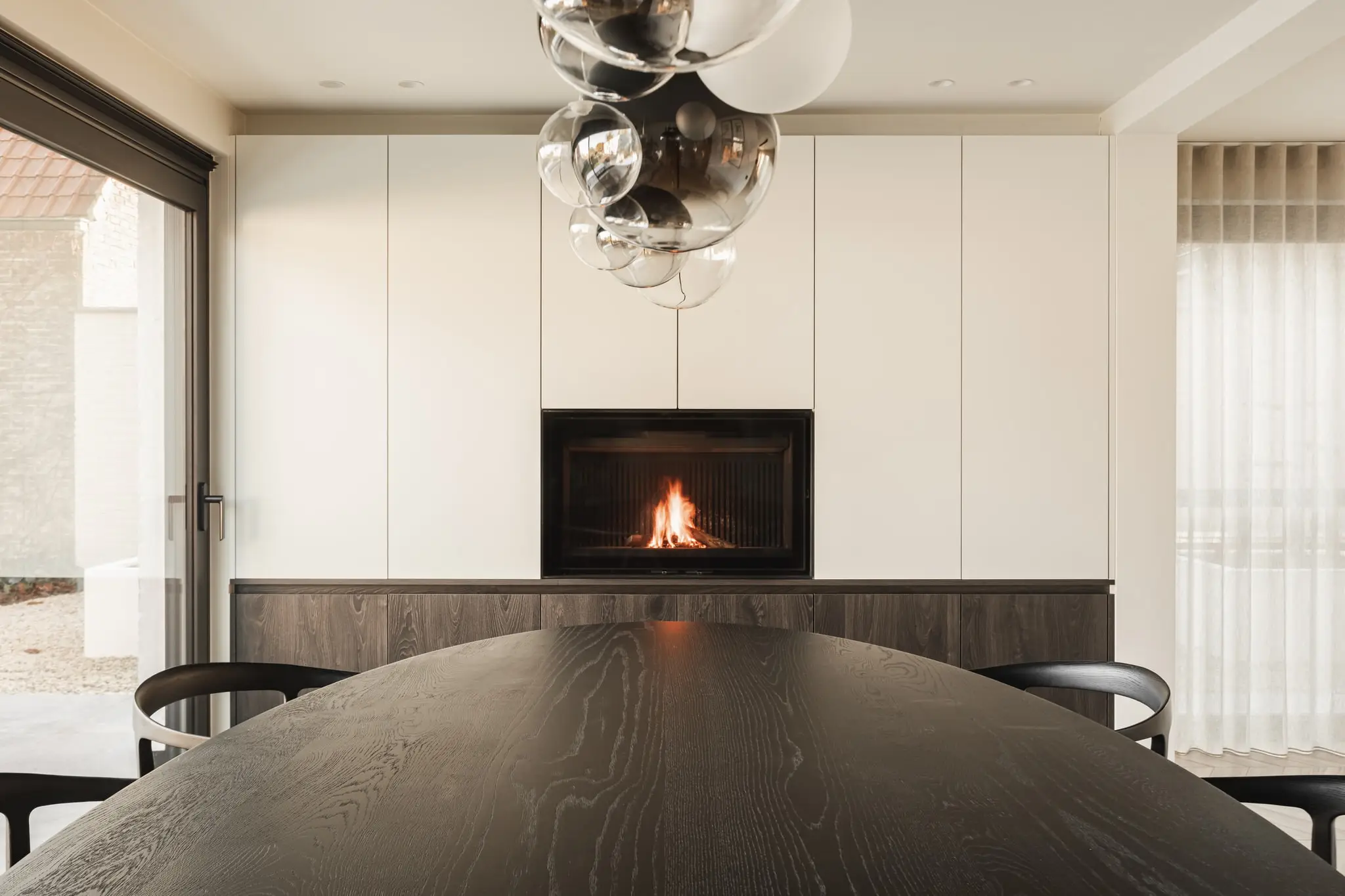 Eetkamer met een ovale tafel en een haard in een witte kastenwand