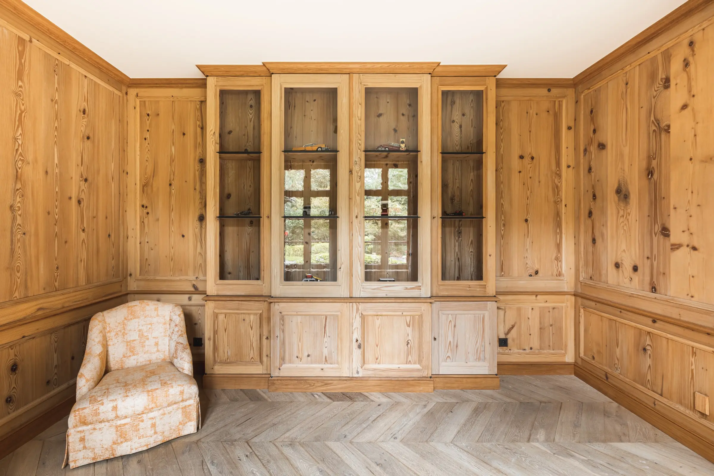 Kamer met houten lambrisering, ingebouwde glazen kasten en een fauteuil