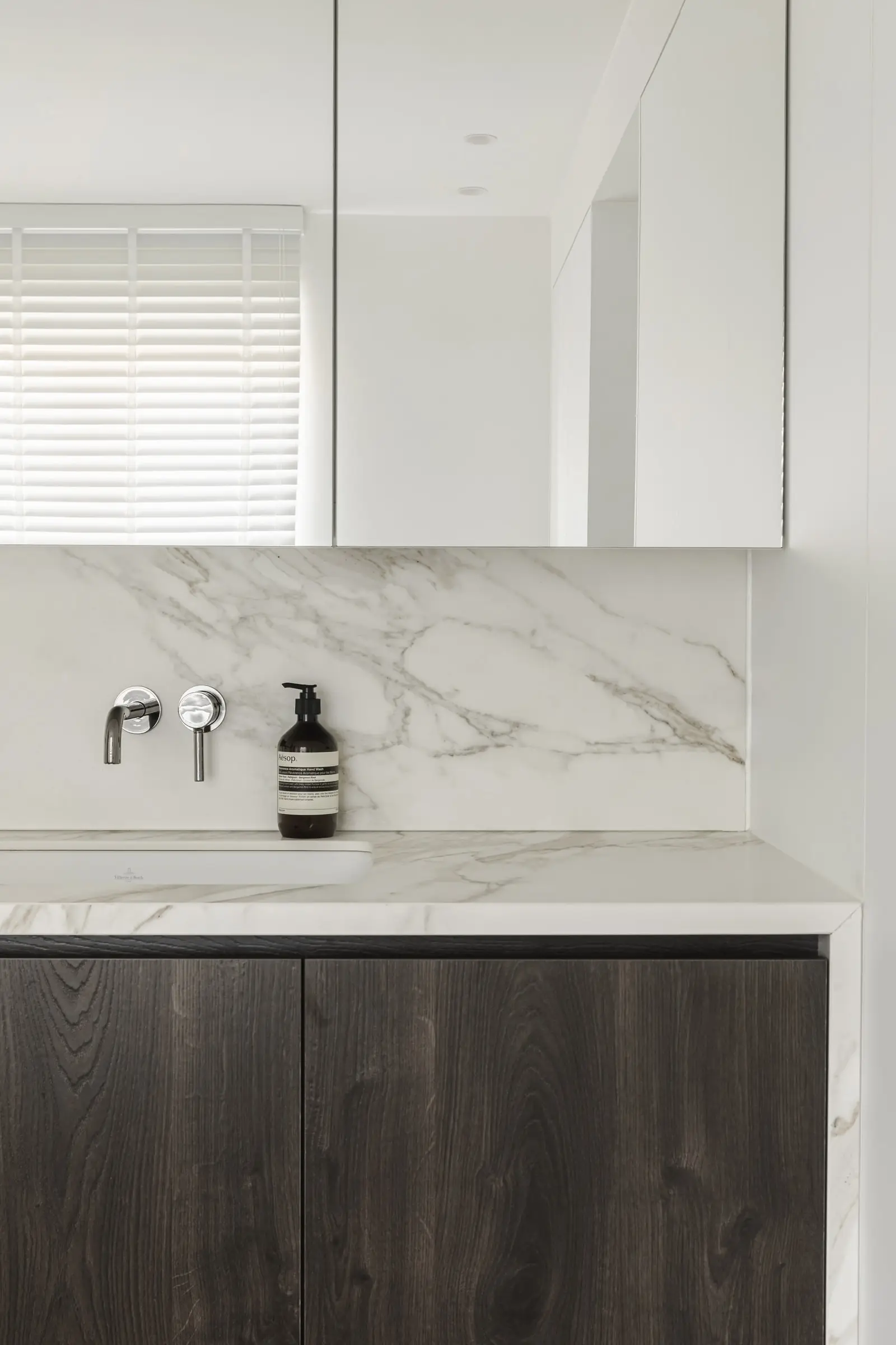 Lavabo met een marmeren achterwand en een donkere houten kast
