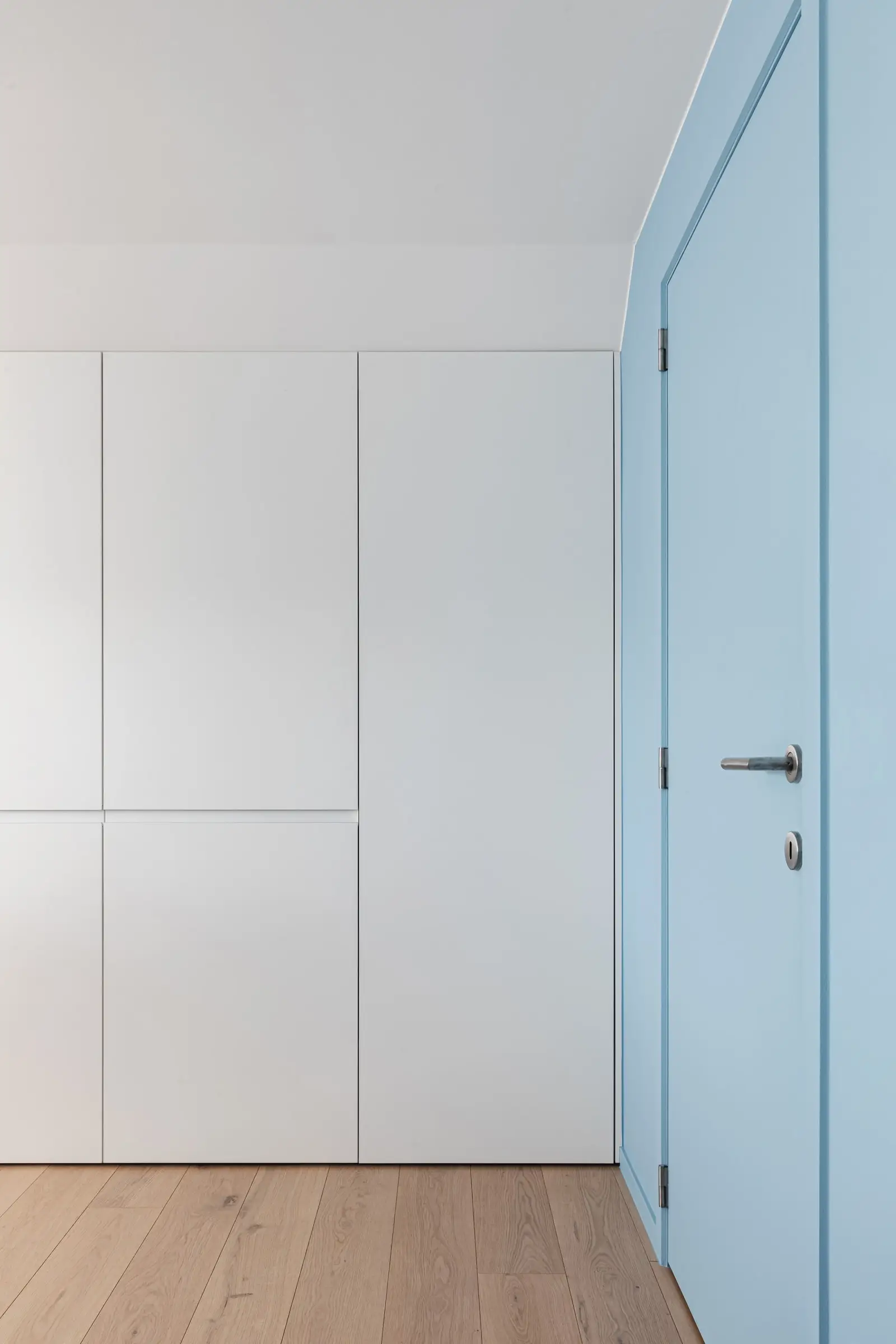 Lichtblauwe muur en deur naast witte kasten