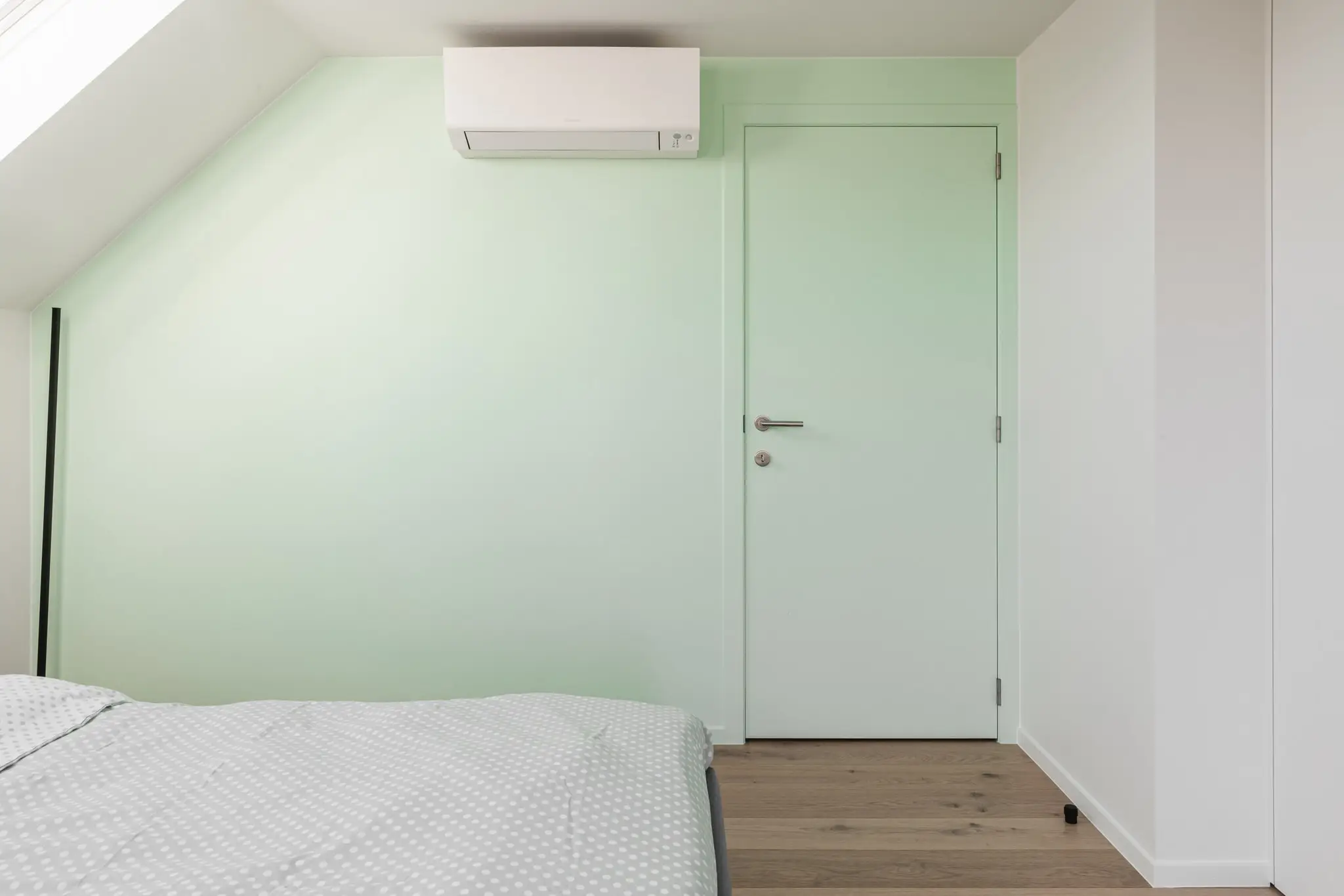 Slaapkamer onder het dak met een mintgroene muur en een witte deur