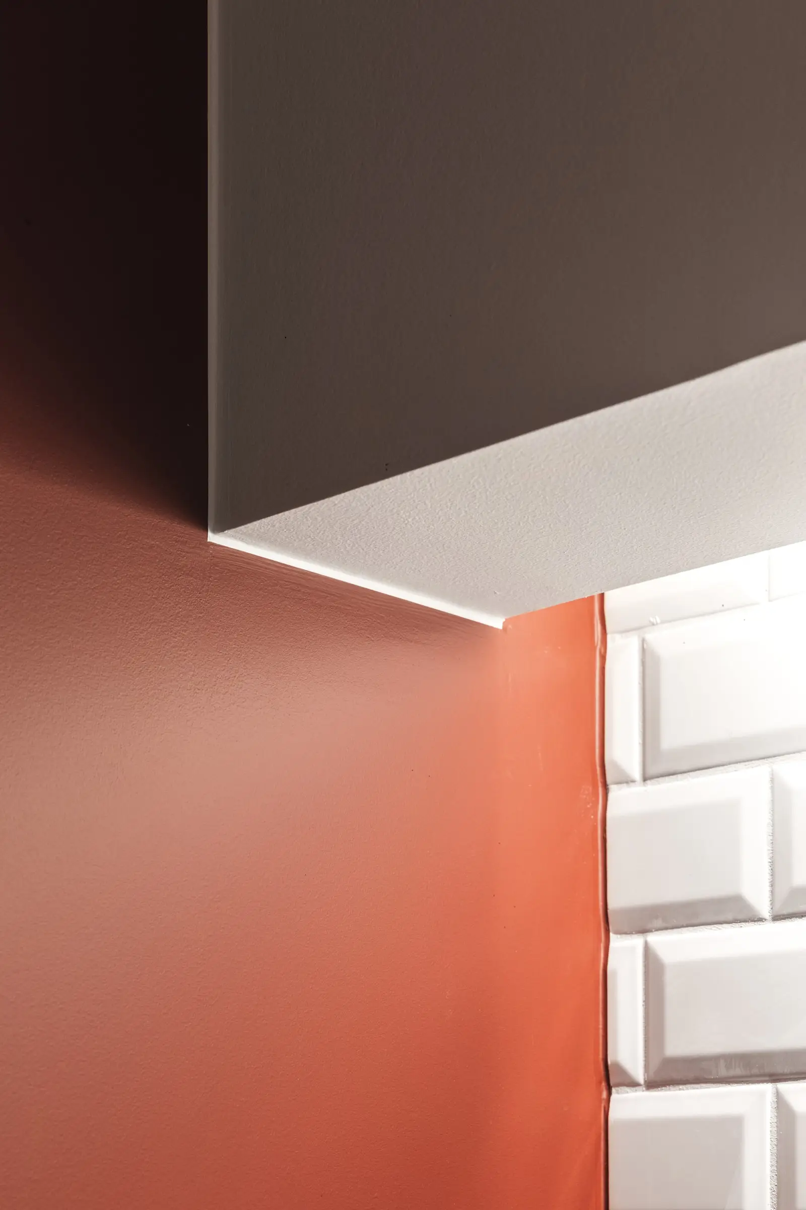 Detail van een rode muur, witte tegels en een donker plafondvlak