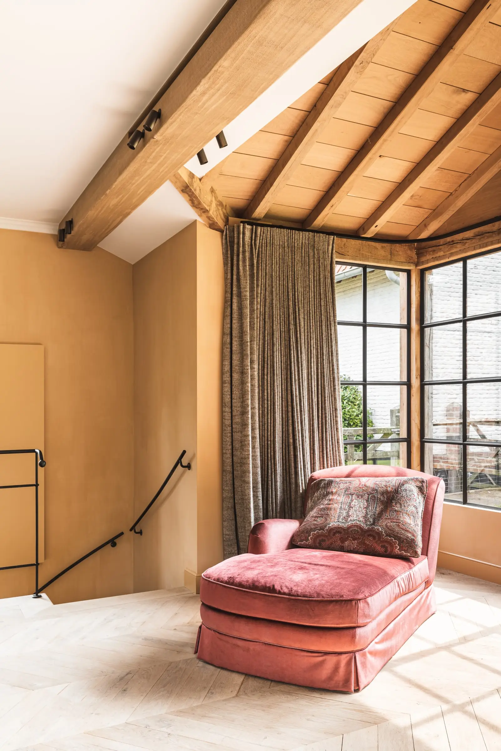 Hoek van de serre met een roze chaise longue onder een houten plafond