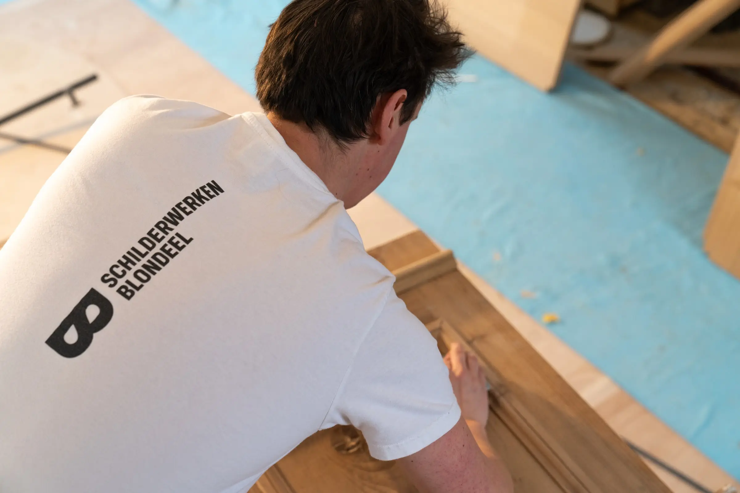 Timothy Blondeel werkt geknield aan een houten kader op een afgedekte vloer