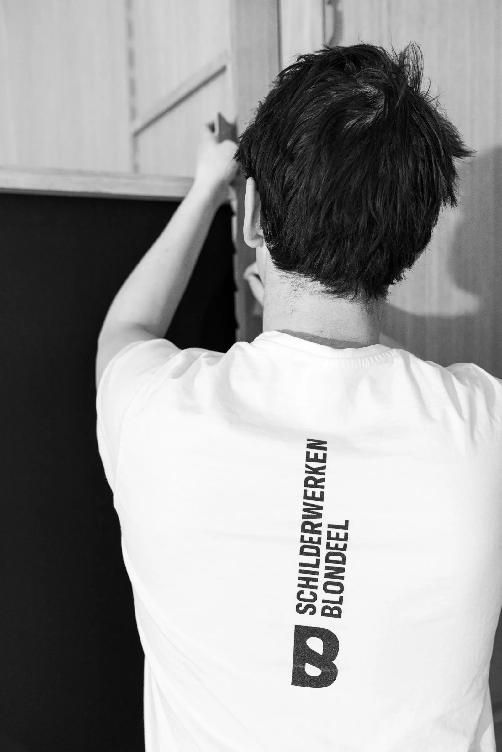 Timothy Blondeel aan het werk, op de rug van zijn T-shirt het logo van Schilderwerken Blondeel, in zwart-wit
