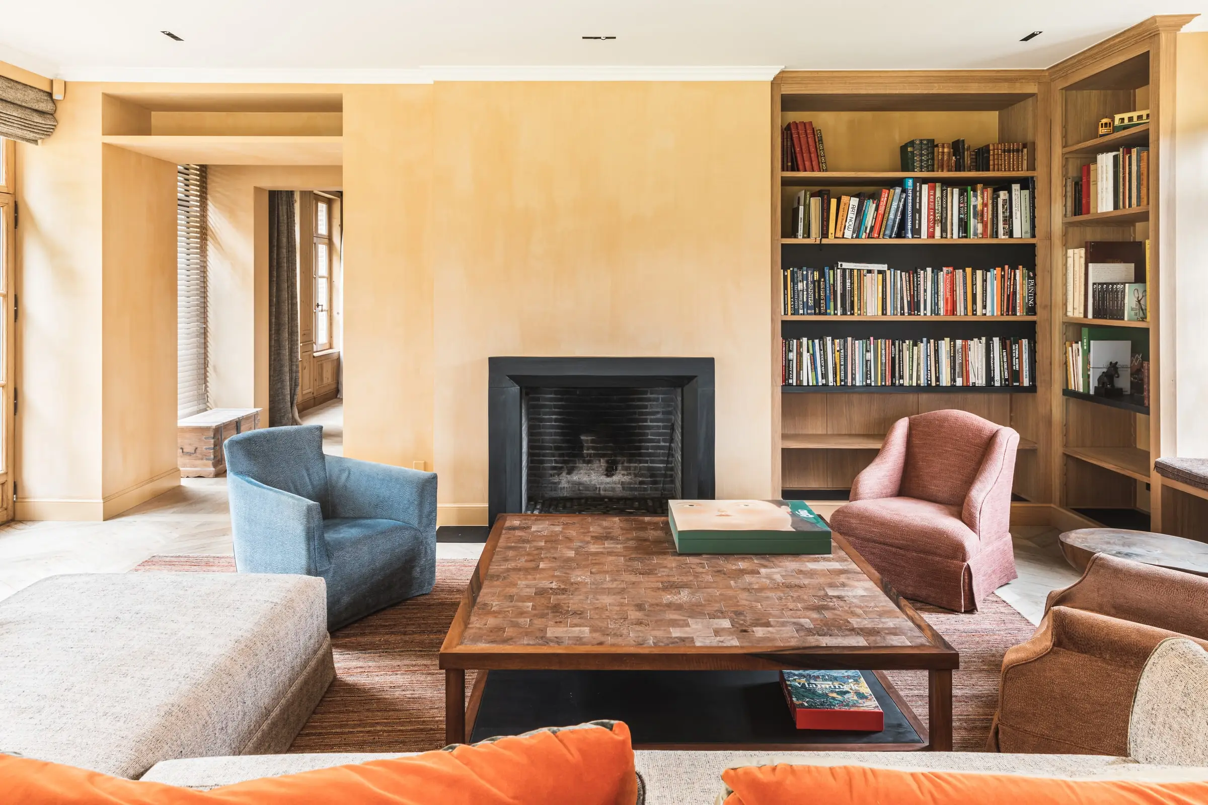 Woonkamer met okerkleurige muren, een open haard met een zwarte omkadering en houten boekenkasten